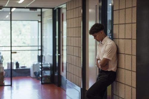 A side view of a young teenage boy who is looking troubled in a school hallway